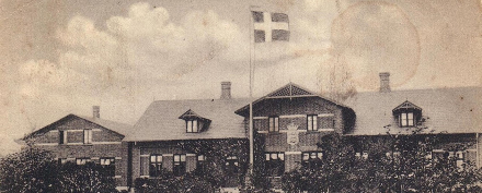 Postcard depicting Vester Vedsted Efterskole from the early 1900s. The Danish symbolism with Dannebrog in the garden and the coat of arms on the gable is strong. Photo: Lokalhistorisk Arkiv for Vester Vedsted Sogn.